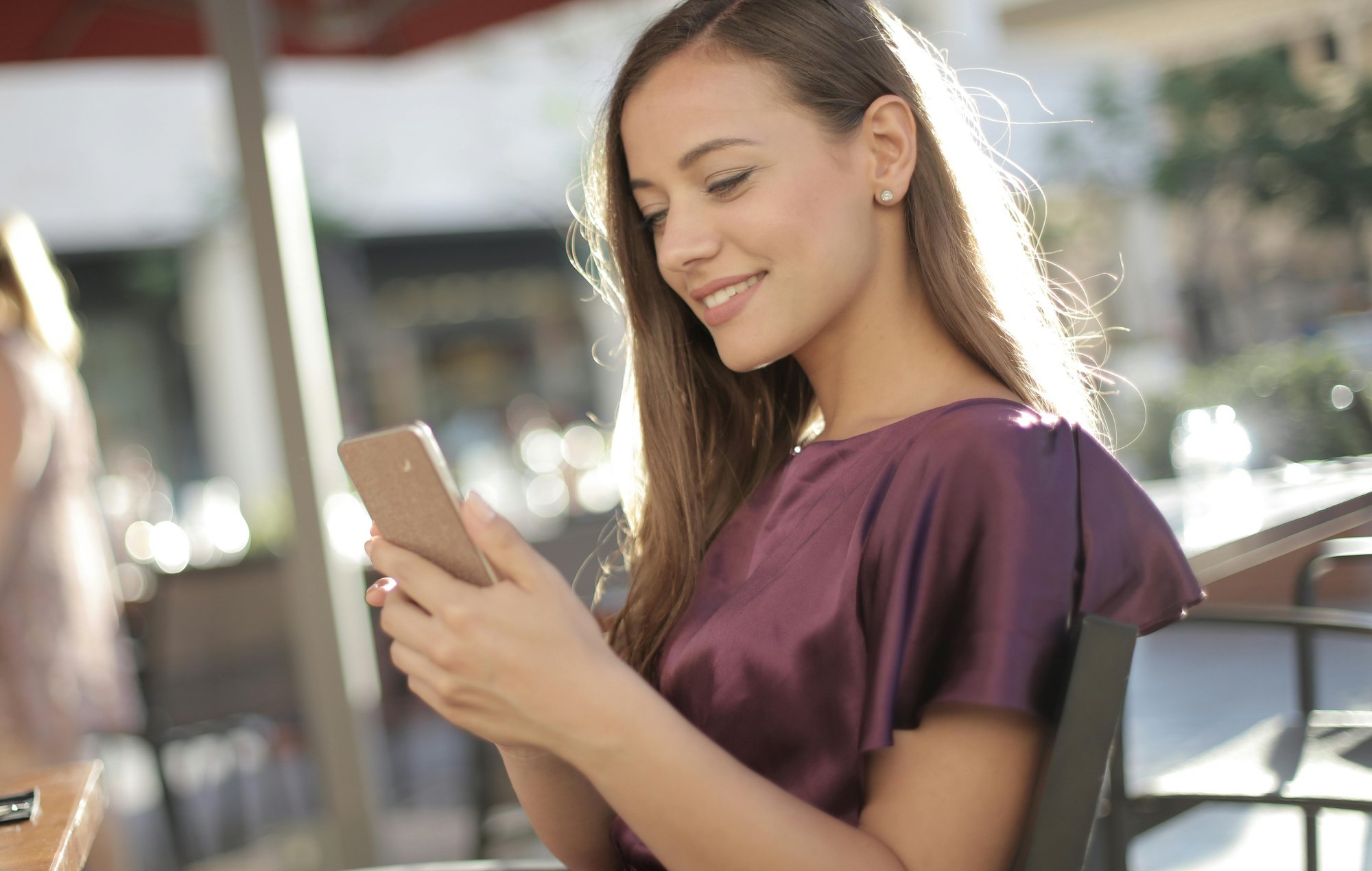 Lady on phone outside in the sun sitting at a table